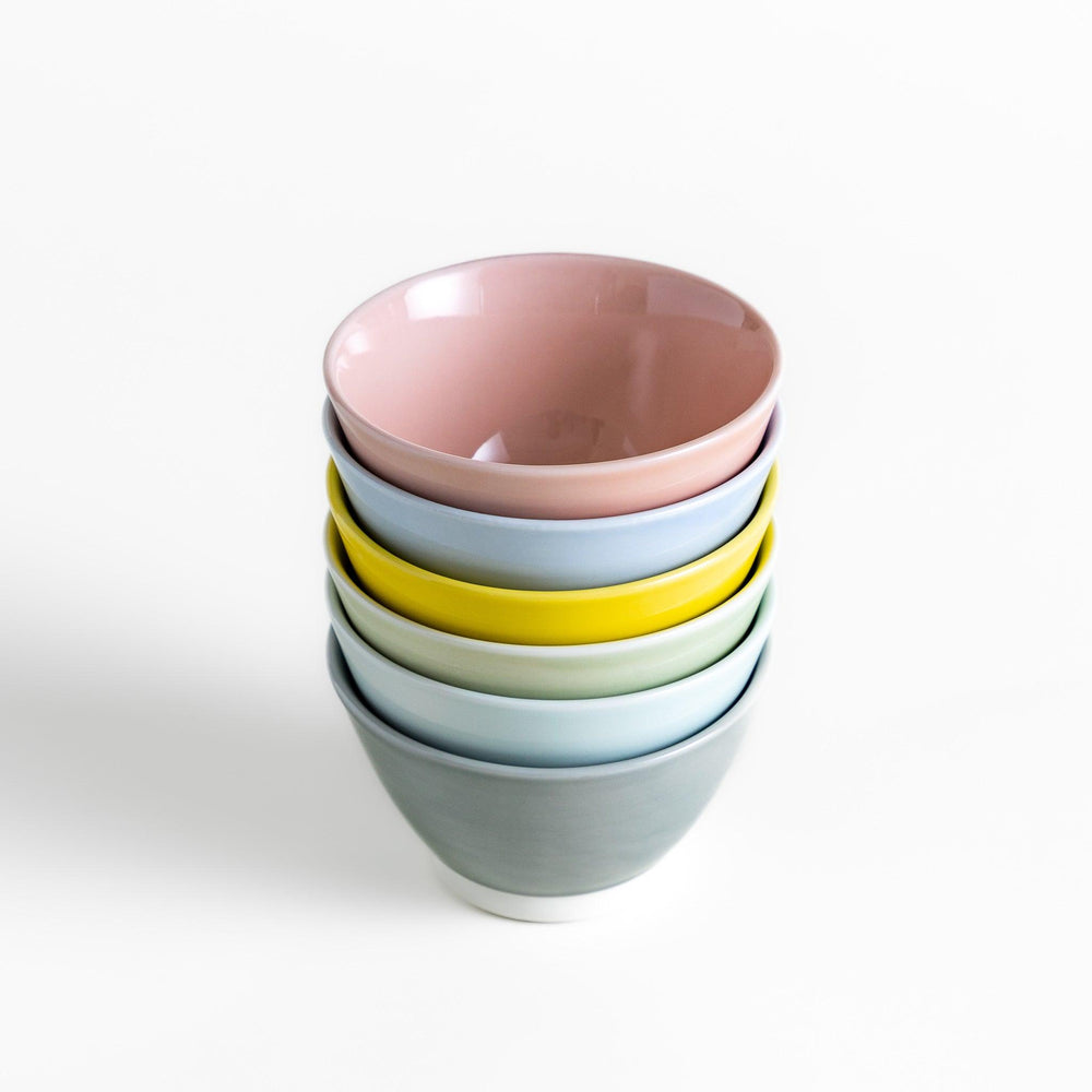 A stack of six pastel-colored dessert bowls in pink, blue, yellow, green, white, and gray, each with a smooth finish, perfect for adding a soft touch to your table setting.