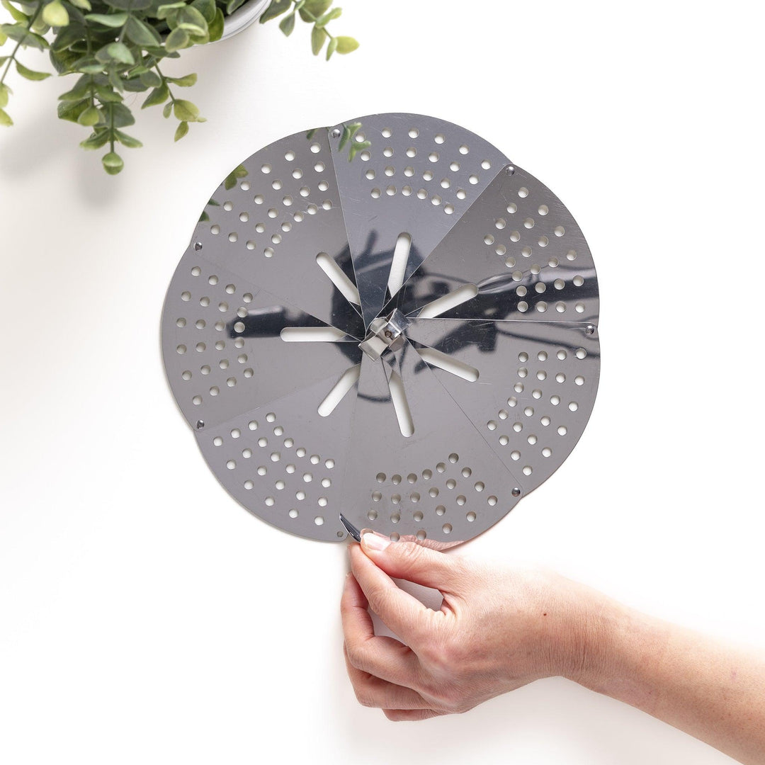 Hand adjusting a stainless steel drop lid with foldable petals, a versatile kitchenware tool for steaming and simmering in various pot sizes.